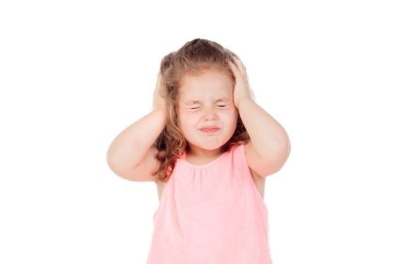 3 year old toddler looking angry and covering her ears with eyes closed, about to have a tantrum
