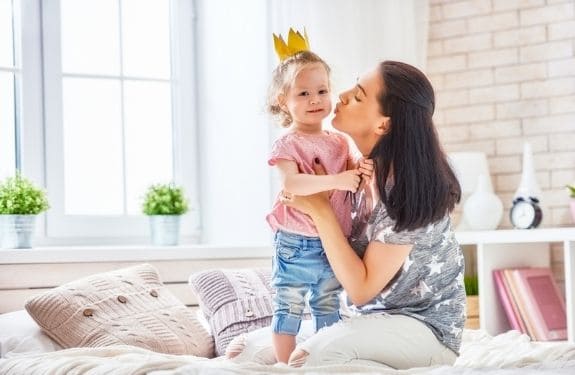 Mom and daughter sitting on floor, mom about to kiss daughter on cheek