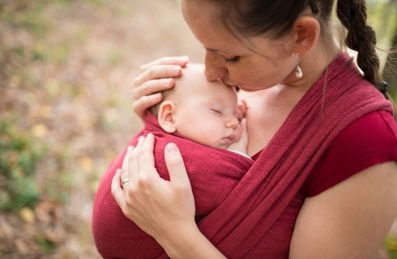 Mom kissing baby's head, the baby is in a baby wrap/carrier