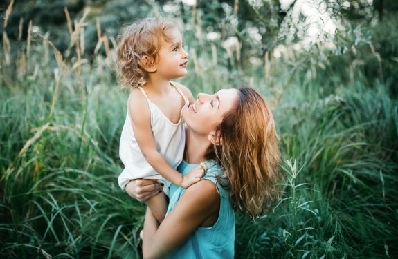 Mom outside holding up daughter, both happy smiling