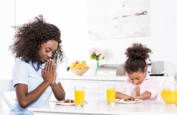 mom and daughter praying at breakfast table
