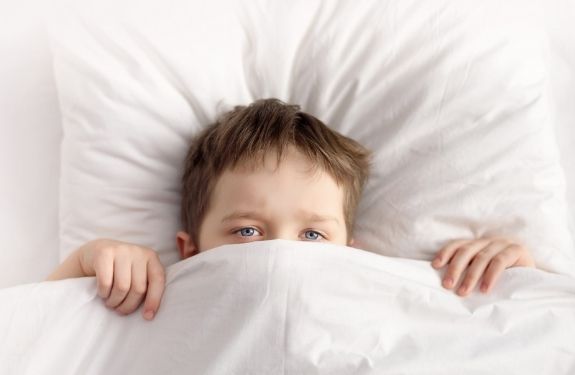 kid in bed with cover up to his eyes
