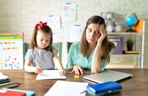 mom looking frustrated while child writes on paper at table