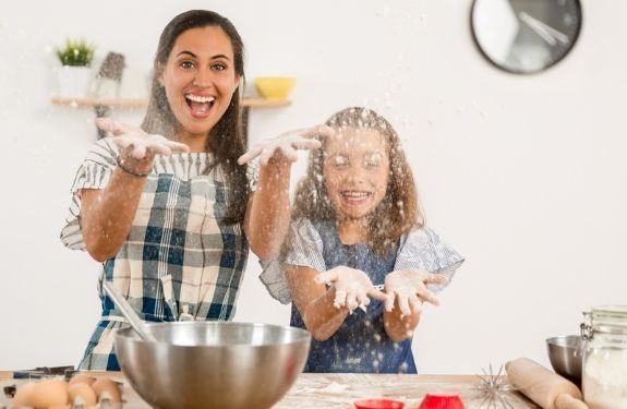 mom and daughter smiling throwing flour while baking