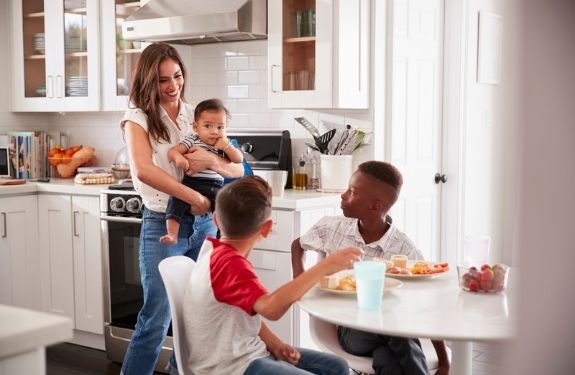 mom holding baby smiling and son and friend sitting at table